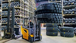 Vue d'un entrepôt de pneus avec de hauts rayonnages et un chariot élévateur avec des pneus chargés