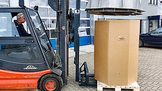 A red forklift truck takes a large cylindrical roll on a pallet onto the fork
