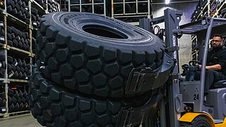 A forklift lifts and rotates two large tyres using a double tyre clamp in a store house
