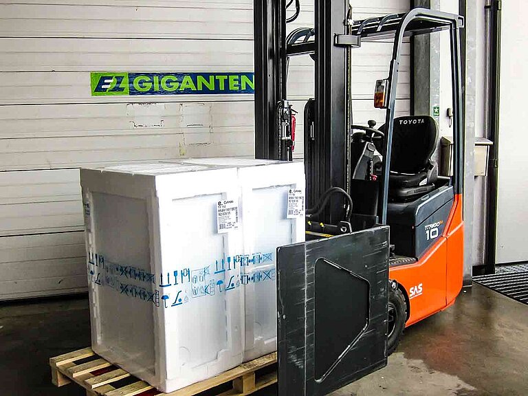 Forklift truck with goods packed in polystyrene on a wooden pallet in front of a roller shutter door