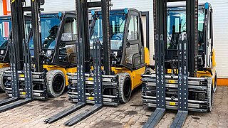 Several forklifts, equipped with identical clamping forks, are parked in a row
