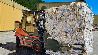 A red forklift truck holds a large cube of pressed waste paper in a bale clamp