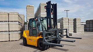 A yellow forklift truck with a special, wide double brick clamp in front of stored bricks