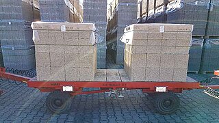 A small trailer with two loaded stone packages stands in front of packages with building materials