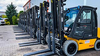 A fleet of yellow forklifts stands in a row in front of the rolling doors of a warehouse