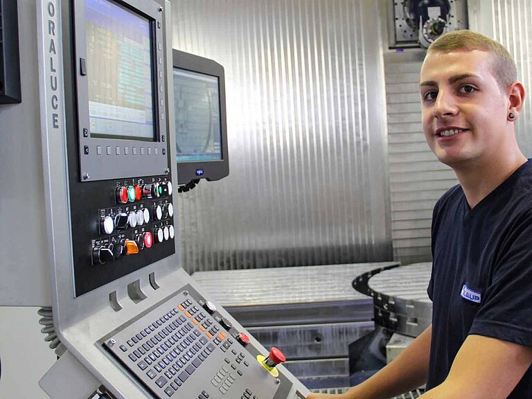 Ein junger Mann mit KAUP T-Shirt bedient das Interface einer Fertigungsmaschine