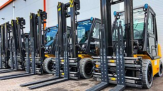 Several yellow forklifts with identical attachments are lined up next to each other
