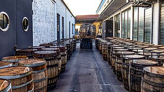 A forklift truck moves through a narrow aisle lined with wooden barrels of spirits