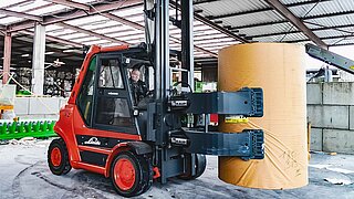 A red forklift lifts and transports a cylindrical bale with a bale clamp in vertical position