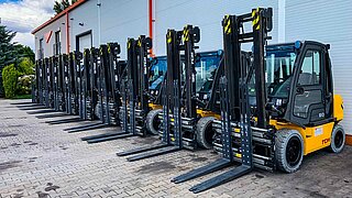 Several forklifts, equipped with identical clamping forks, are parked in a row