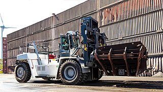 Eine große Baumaschine transportiert einen Schlackecontainer mit einem speziellen Anbaugerät