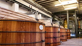 Blick auf vier große Holzbottiche zur Whiskey-Lagerung in einer Spirituosen-Brennerei