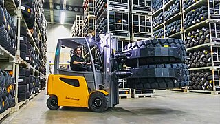 A forklift lifts two large tyres horizontally on top of each other with the help of a round clamp