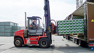 Une machine rouge manœuvre plusieurs palettes de caisses de bière sur le plateau d'un camion