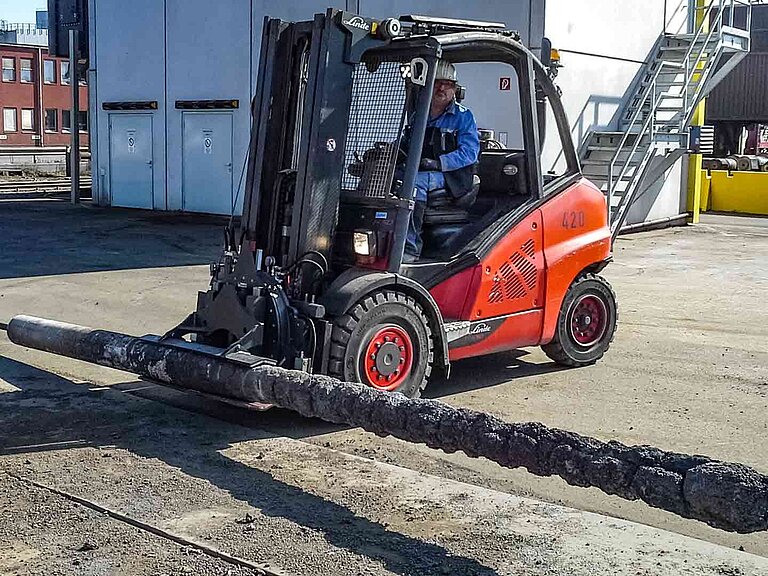 A red forklift truck holds a metal concrete lance in a special rotating roller clamp