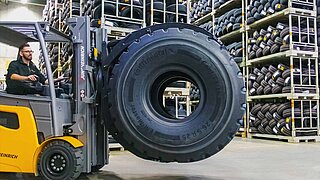 A yellow forklift truck transports two large tyres side by side with a tyre clamp