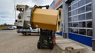 A forklift truck lifts a cylindrical box with a special rotatable attachment