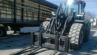 Une machine de construction avec déplacement latéral devant un camion avec plateau de chargement