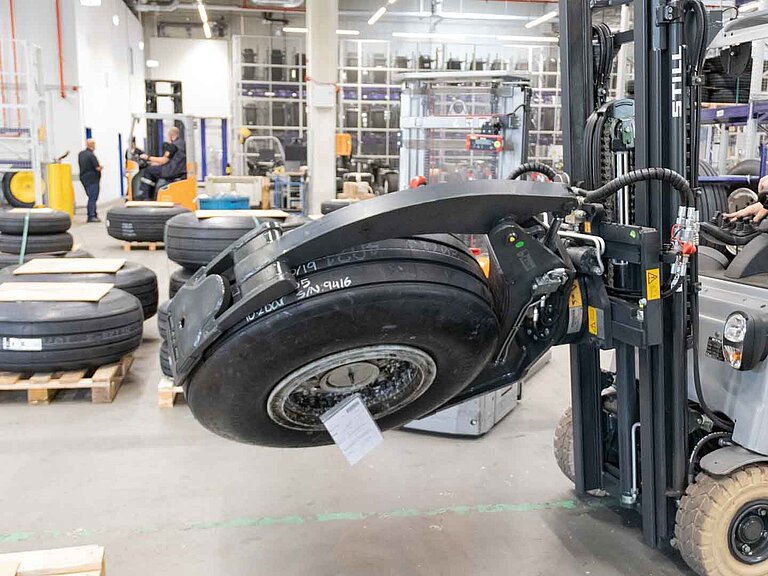 A forklift truck rotates and transports an aircraft tyre with the help of a tyre clamp