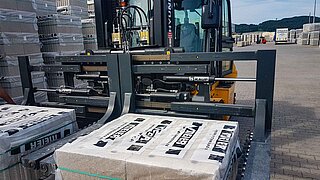 A forklift truck with a special, wide double stone clamp transports packed stones