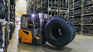 A forklift truck transports a large tyre vertically with the help of a KAUP roller clamp