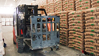 Red forklift truck with push-pull attachment manoeuvres through mountains of brown bags