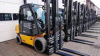 A fleet of yellow forklifts with identical attachments are lined up in a row