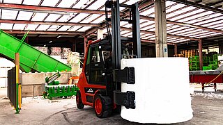 A forklift truck transports a large roll of paper with the help of a KAUP bale clamp