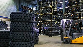 A yellow forklift truck with tyre clamp navigates through a tyre warehouse with high racks